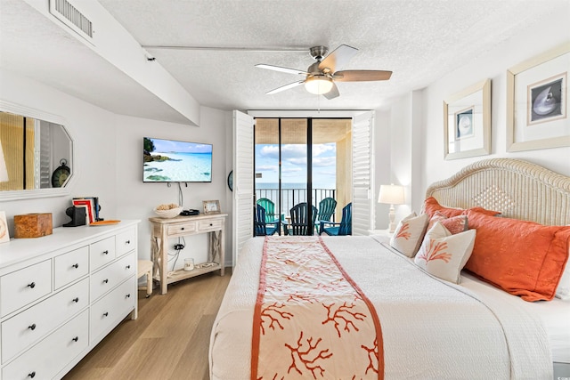 bedroom featuring access to exterior, ceiling fan, a wall of windows, light hardwood / wood-style flooring, and a textured ceiling