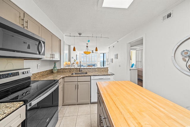 kitchen featuring sink, wood counters, a textured ceiling, light tile patterned floors, and appliances with stainless steel finishes