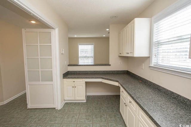 kitchen with a textured ceiling, built in desk, white cabinetry, and dark tile patterned floors