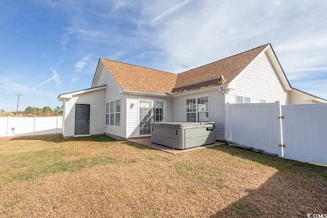 back of house with a hot tub and a lawn