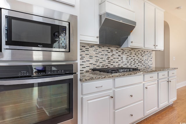 kitchen with stone countertops, white cabinets, decorative backsplash, stainless steel appliances, and light wood-type flooring