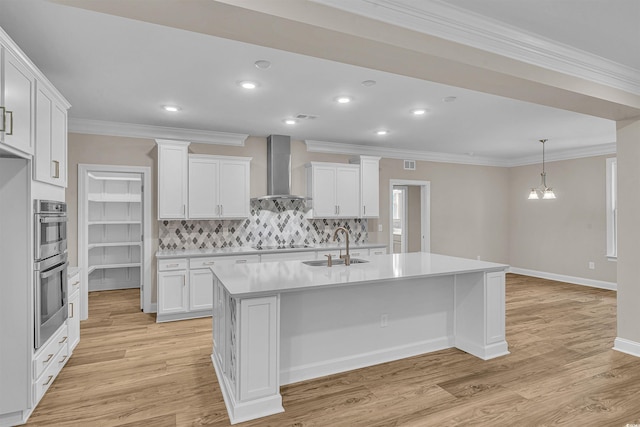 kitchen featuring light hardwood / wood-style floors, white cabinetry, a center island with sink, and wall chimney range hood