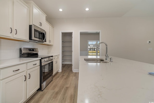 kitchen with sink, appliances with stainless steel finishes, light hardwood / wood-style floors, light stone counters, and white cabinetry