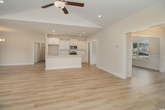 unfurnished living room with ceiling fan with notable chandelier, light hardwood / wood-style floors, and high vaulted ceiling