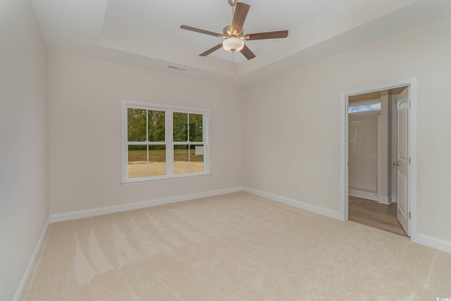 spare room with a tray ceiling, ceiling fan, and light colored carpet