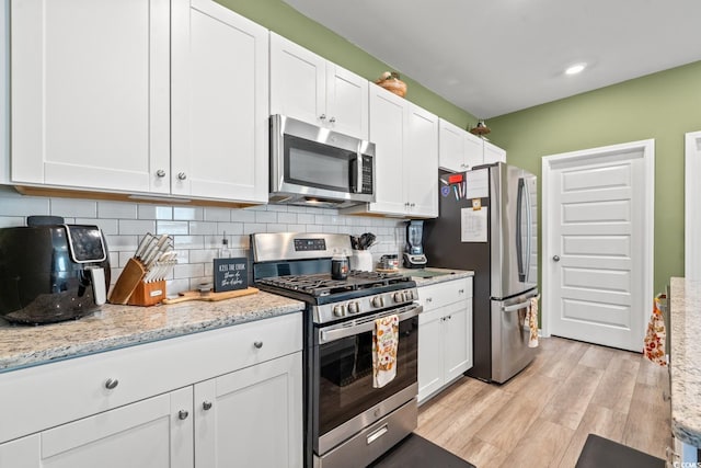 kitchen with white cabinets, stainless steel appliances, light hardwood / wood-style flooring, and light stone countertops