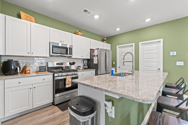 kitchen with white cabinetry, sink, stainless steel appliances, an island with sink, and a kitchen bar