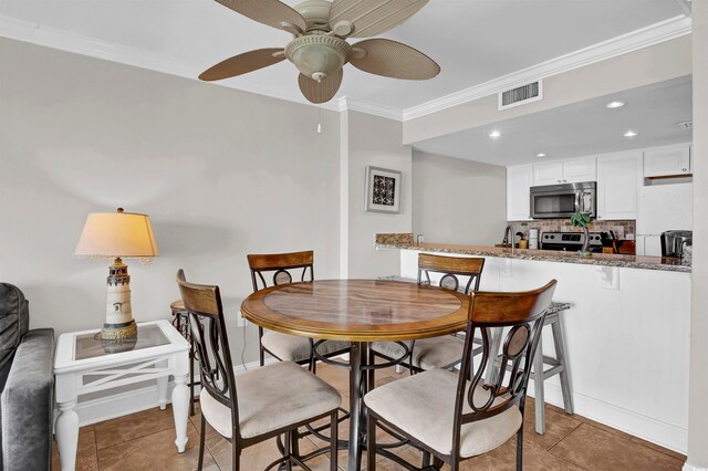 tiled dining room with ceiling fan and crown molding