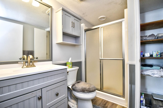 bathroom with wood-type flooring, a textured ceiling, toilet, a shower with door, and vanity