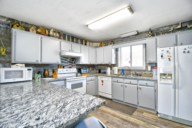 kitchen featuring white appliances, sink, light hardwood / wood-style flooring, light stone countertops, and a textured ceiling