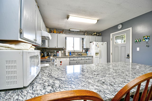 kitchen featuring kitchen peninsula, decorative backsplash, white appliances, and a textured ceiling