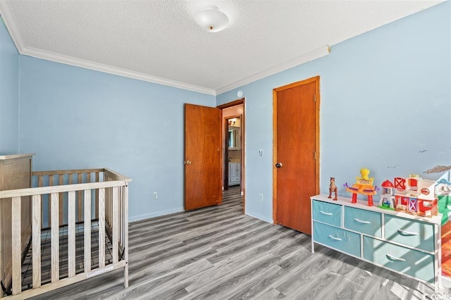 bedroom featuring a textured ceiling, ornamental molding, a crib, and hardwood / wood-style flooring