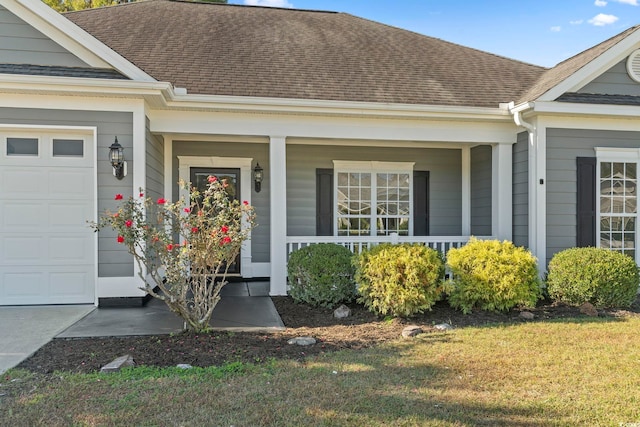 view of exterior entry with covered porch, a garage, and a lawn