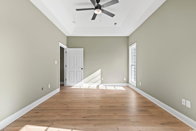 spare room featuring a tray ceiling, ceiling fan, and light hardwood / wood-style flooring