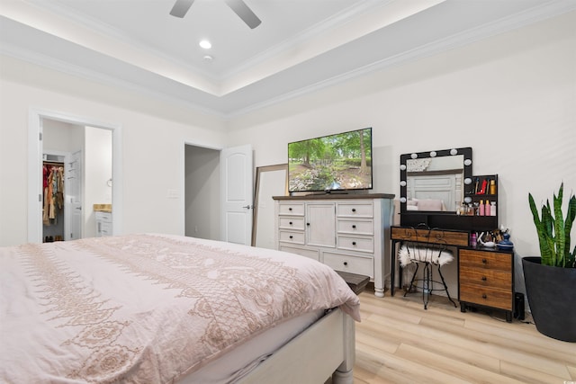 bedroom featuring ensuite bath, ceiling fan, a raised ceiling, crown molding, and light wood-type flooring