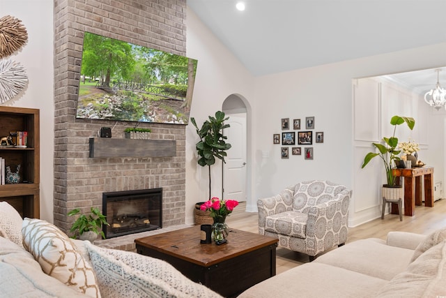 living room featuring a brick fireplace, high vaulted ceiling, and light wood-type flooring