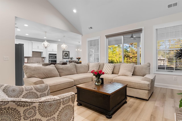 living room with ceiling fan with notable chandelier, light hardwood / wood-style floors, and high vaulted ceiling