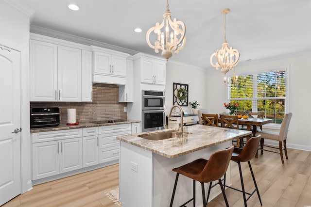 kitchen featuring sink, light hardwood / wood-style flooring, a chandelier, a kitchen island with sink, and white cabinets