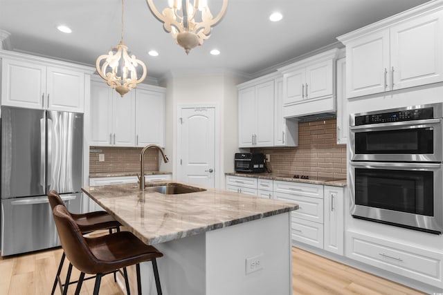 kitchen featuring light stone countertops, pendant lighting, a kitchen island with sink, white cabinets, and appliances with stainless steel finishes