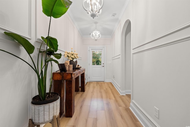 doorway to outside with a chandelier, light wood-type flooring, and ornamental molding