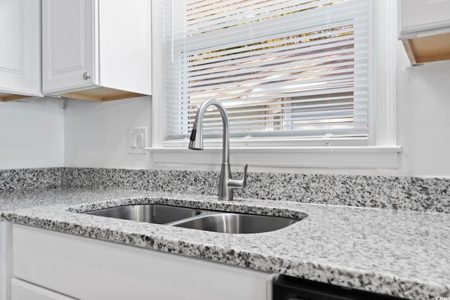 kitchen featuring white cabinets, light stone counters, and sink