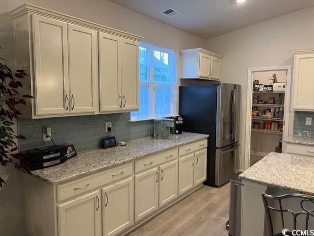 kitchen featuring light stone countertops, stainless steel refrigerator with ice dispenser, decorative backsplash, and light hardwood / wood-style flooring