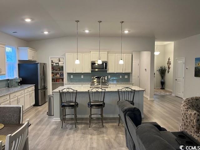 kitchen with lofted ceiling, an island with sink, appliances with stainless steel finishes, tasteful backsplash, and decorative light fixtures