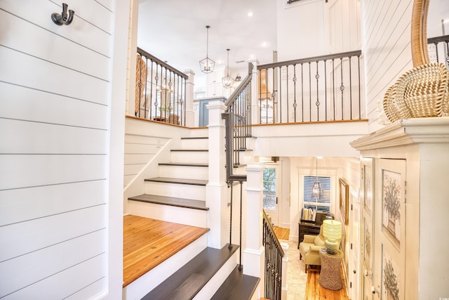 stairway with a towering ceiling, hardwood / wood-style floors, and a chandelier