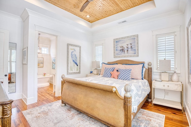 bedroom with a tray ceiling, multiple windows, and light wood-type flooring