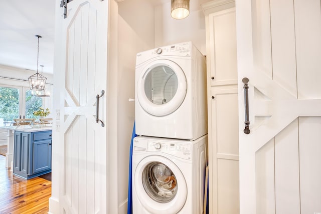 laundry area featuring a barn door, stacked washing maching and dryer, and light hardwood / wood-style floors