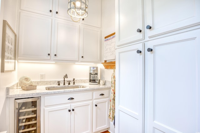 kitchen featuring light stone counters, sink, beverage cooler, and white cabinets