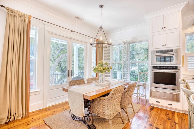 dining space with an inviting chandelier, ornamental molding, light hardwood / wood-style floors, and french doors