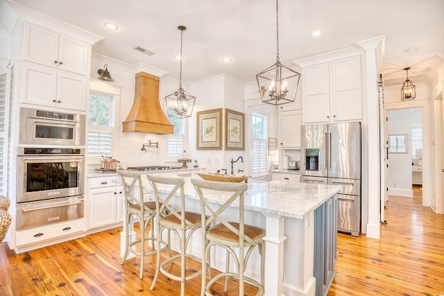 kitchen with a breakfast bar area, white cabinetry, appliances with stainless steel finishes, pendant lighting, and a kitchen island with sink