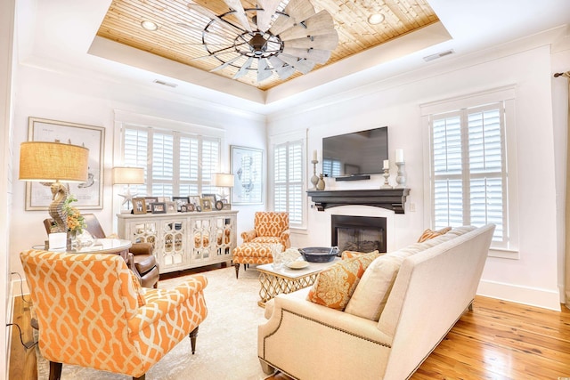 living room featuring crown molding, light wood-type flooring, and a tray ceiling