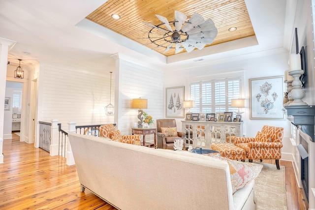 living room featuring ornamental molding, light hardwood / wood-style flooring, wood ceiling, and a tray ceiling