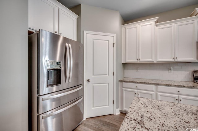 kitchen with white cabinetry, light stone countertops, stainless steel refrigerator with ice dispenser, backsplash, and light wood-type flooring