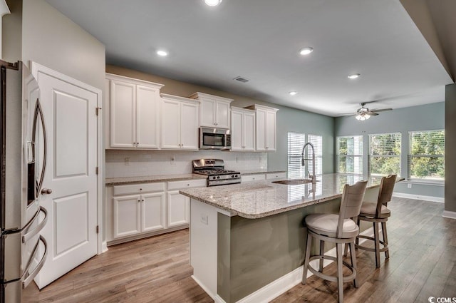 kitchen with white cabinets, sink, stainless steel appliances, and an island with sink