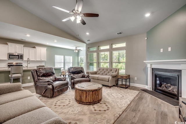 living room with ceiling fan, light hardwood / wood-style flooring, lofted ceiling, and sink