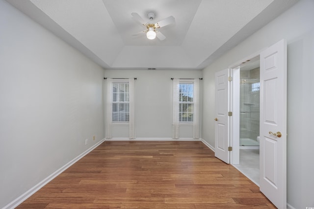 empty room with visible vents, baseboards, a raised ceiling, ceiling fan, and wood finished floors