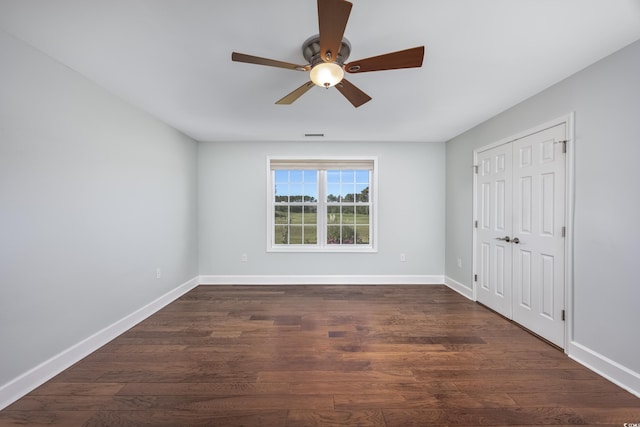 unfurnished bedroom with a closet, dark wood-style flooring, ceiling fan, and baseboards