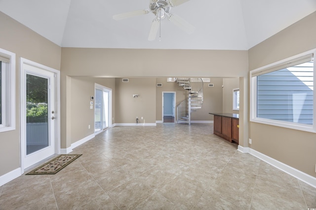 unfurnished living room with high vaulted ceiling, baseboards, and stairway