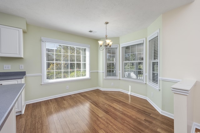 unfurnished dining area with a notable chandelier, visible vents, a textured ceiling, wood finished floors, and baseboards