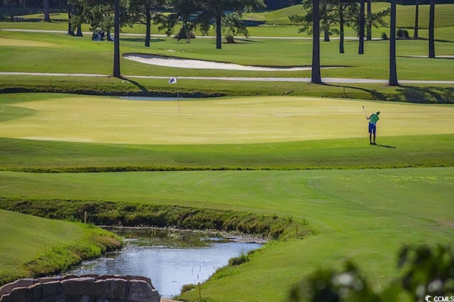 view of community featuring a water view, a lawn, and golf course view