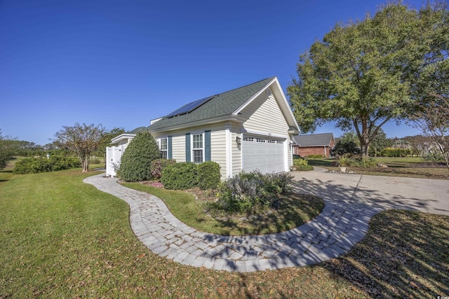 view of side of home with driveway, an attached garage, a lawn, and solar panels