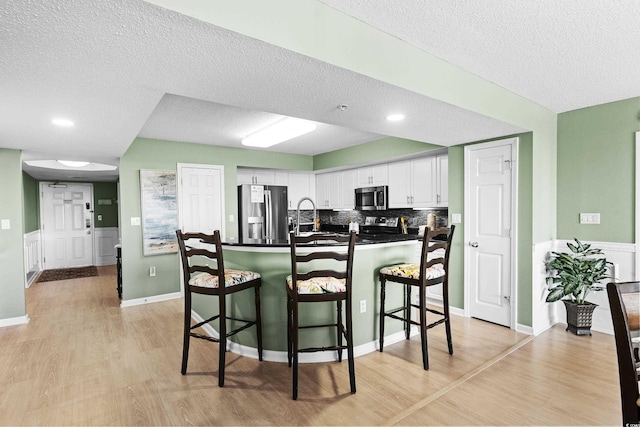 2151 Bridge View Ct Unit 2502, North Myrtle Beach, SC 29582 - kitchen with appliances with stainless steel finishes, a textured ceiling, a breakfast bar area, white cabinetry, and light wood-style flooring
