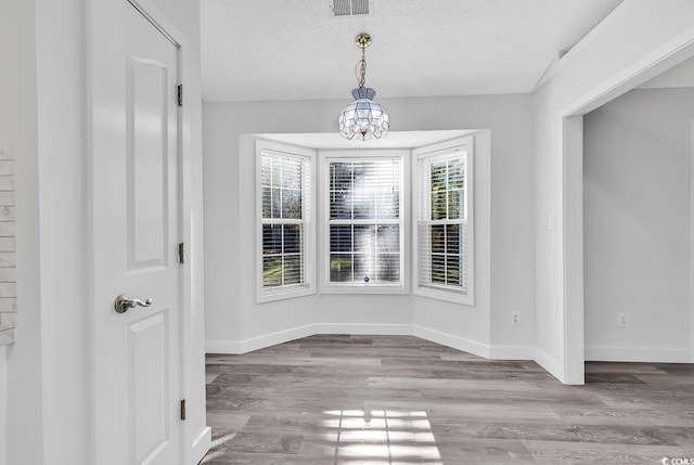 unfurnished dining area with a notable chandelier, light wood-type flooring, and a textured ceiling