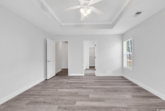 unfurnished bedroom featuring a walk in closet, a raised ceiling, ceiling fan, crown molding, and light hardwood / wood-style floors