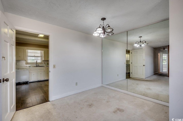 empty room with a textured ceiling, light wood-type flooring, a notable chandelier, and sink