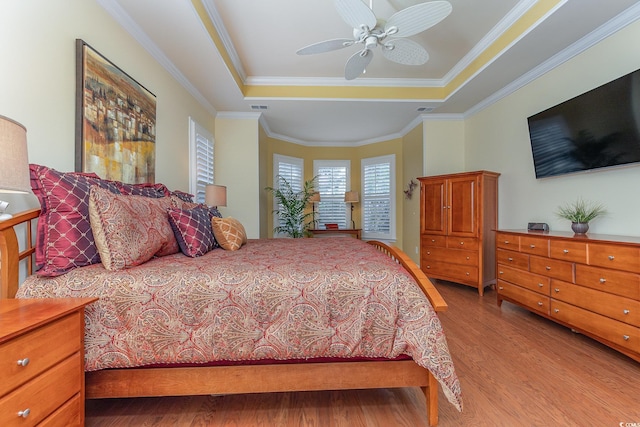 bedroom with ceiling fan, a raised ceiling, light wood-type flooring, and ornamental molding