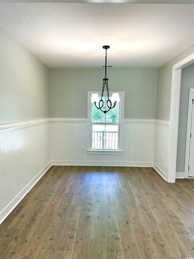 unfurnished dining area featuring a wainscoted wall, visible vents, wood finished floors, and a notable chandelier